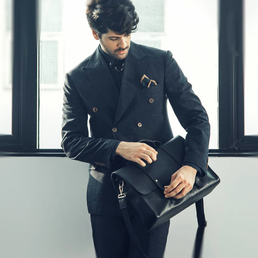 Dressed up model holding a handcrafted leather messenger bag, meticulously hand-crafted by Artimaes artisans.